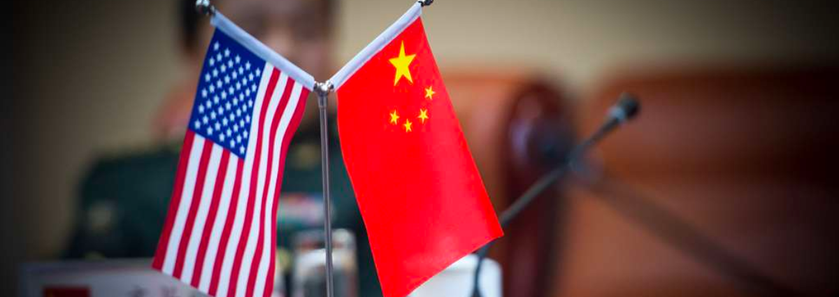 Small U.S. and China flags on a table in the foreground of a meeting